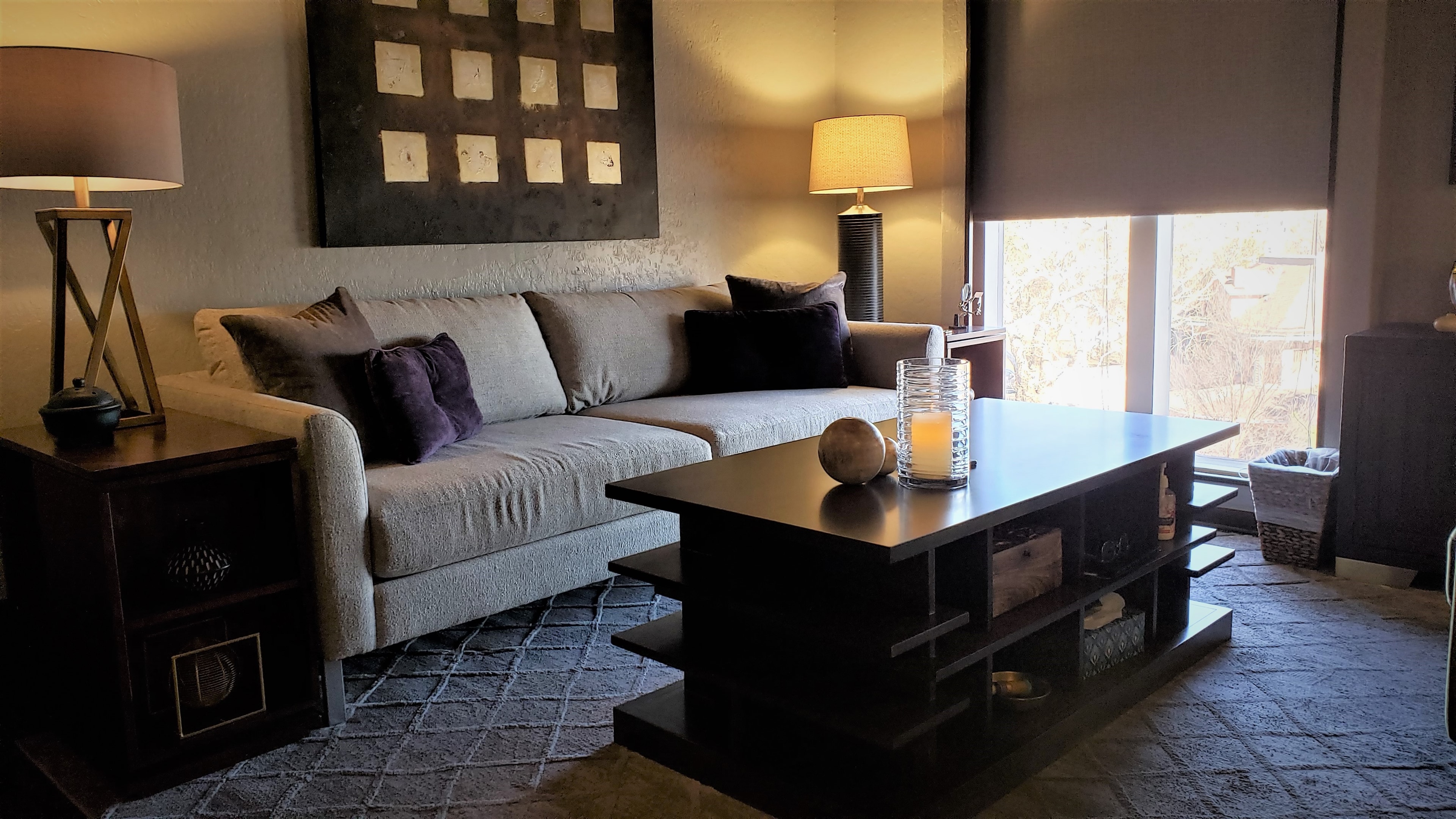 The therapy room — a warm, dimly lit space with a grey sofa, dark coffee table, and lamps